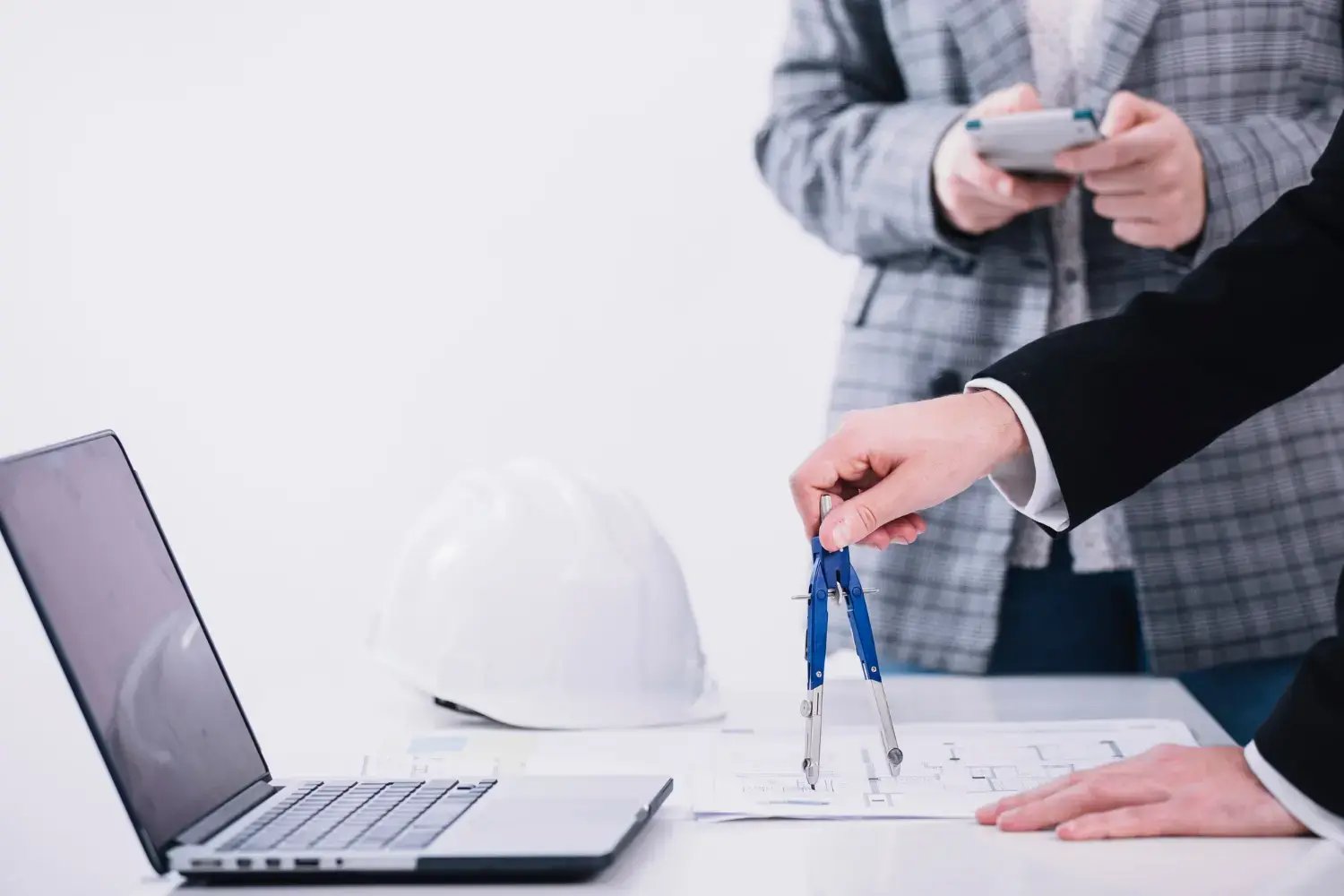 A-person-holding-a-drawing-compass-with-a-white-hard-hat-on-the-table-for-it-support-for-construction-companies